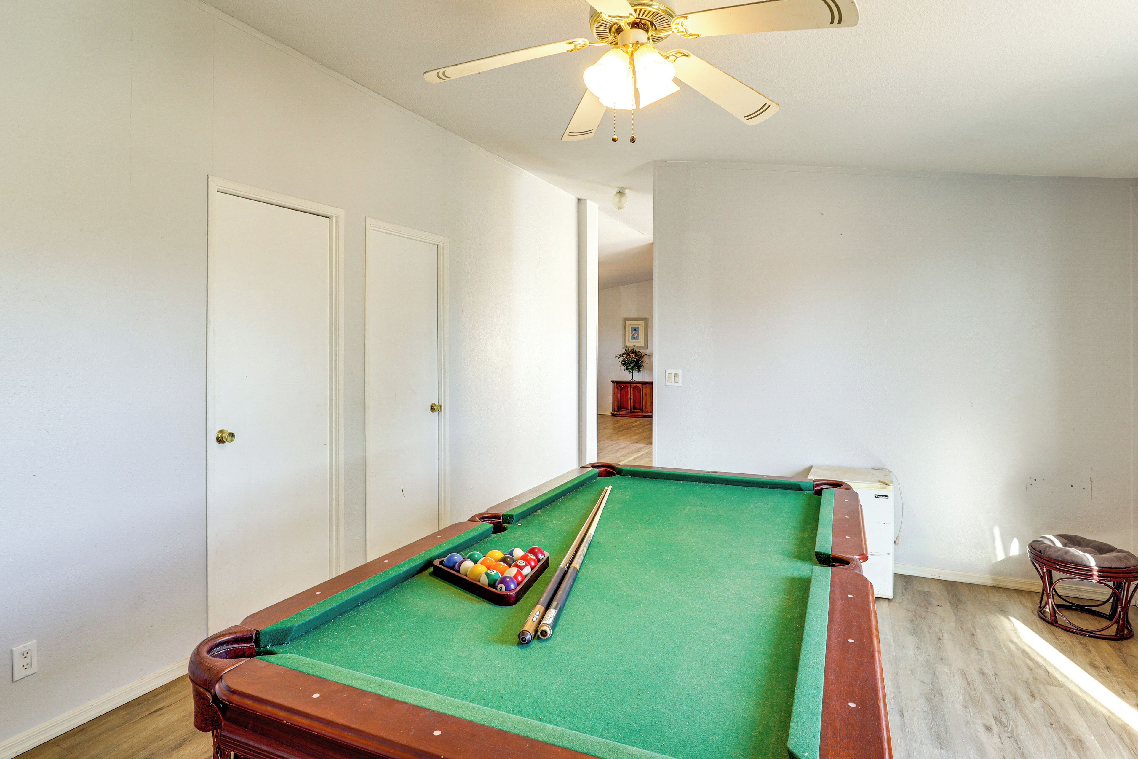 Een pooltafel met ballen en stokken, een plafondventilator en een deur.