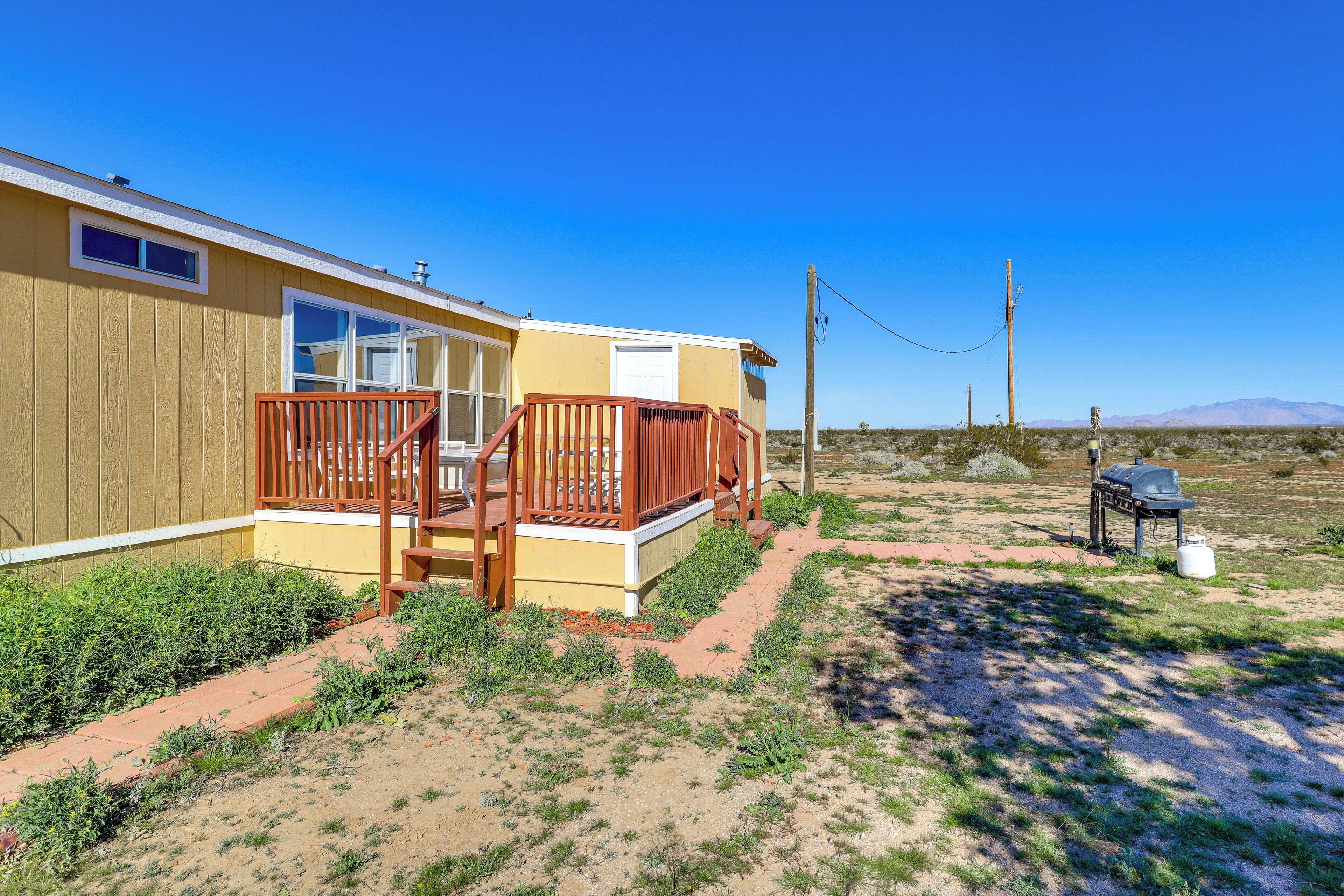 A single-story mobile home with a porch, a barbecue grill, and a water tank.