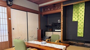 Una habitación japonesa tradicional con suelo de tatami, una mesa de madera baja, sillas verdes y puertas correderas.