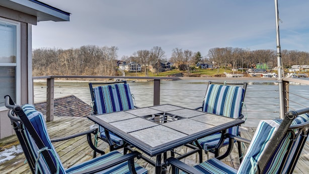 Een terras met een tafel en stoelen, met uitzicht op een waterpartij en huizen op de achtergrond.