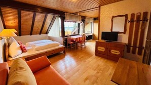 Ein Zimmer mit einem Bett, einer Couch, einem Esstisch mit Stühlen, einem Fernseher und einer Holzbalkendecke.