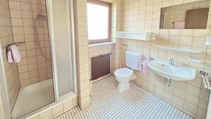 Ein Badezimmer mit Dusche, Toilette, Waschbecken und einem Fenster.