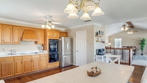 A kitchen with wooden cabinets, stainless steel appliances, a dining table with a centerpiece, and pendant lighting. - 'texoma Shores Hideaway' Family Home w/ Water View (Pottsboro)