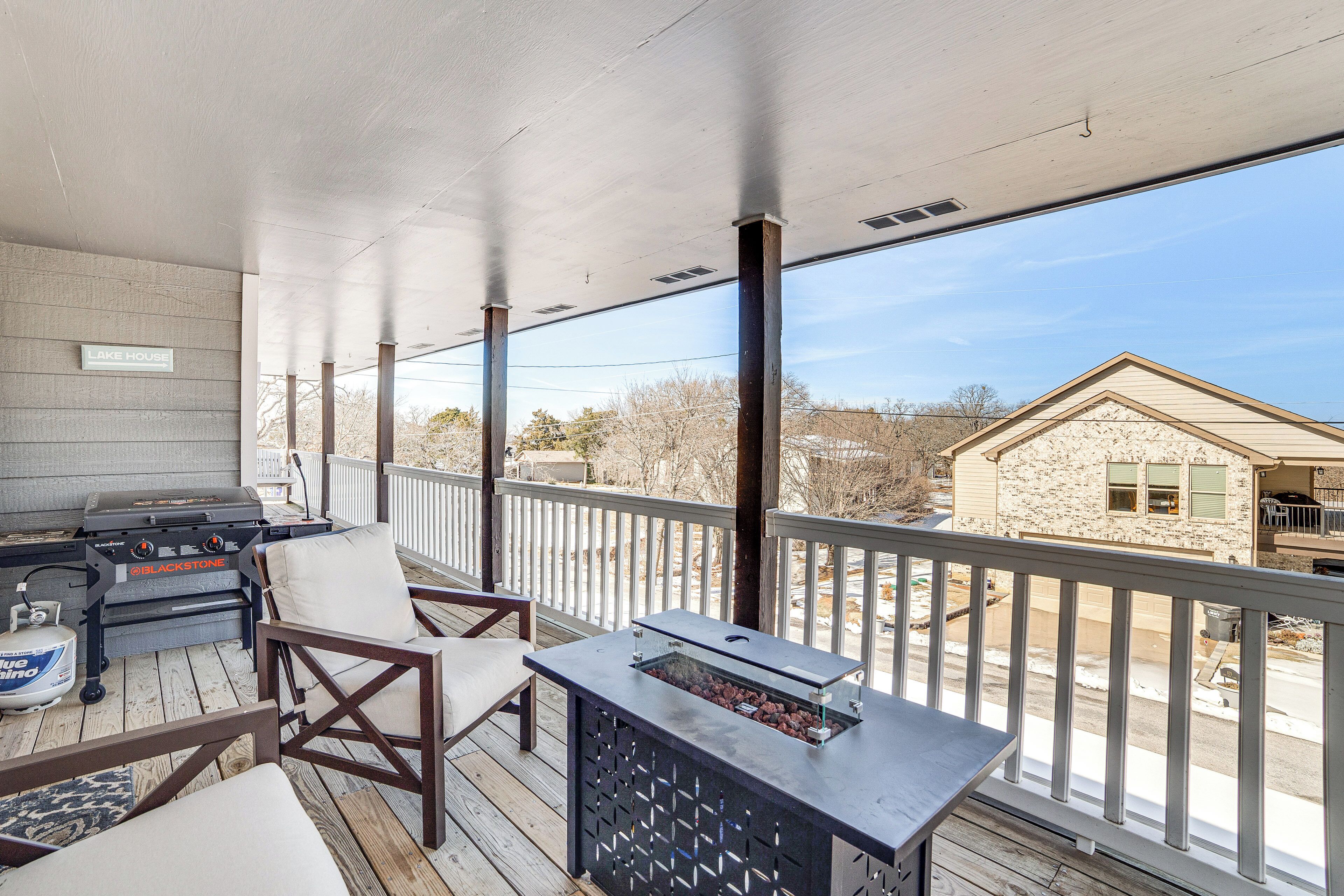 A covered outdoor deck with a grill, chairs, and a table with a fire pit.