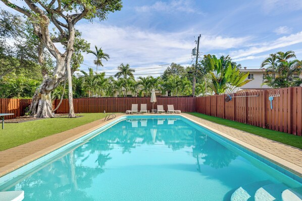 A rectangular swimming pool with a wooden deck, surrounded by a wooden fence, palm trees, and a grassy area. - 3 Mi to Sea! Family Pool House in Fort Lauderdale (Fort Lauderdale)