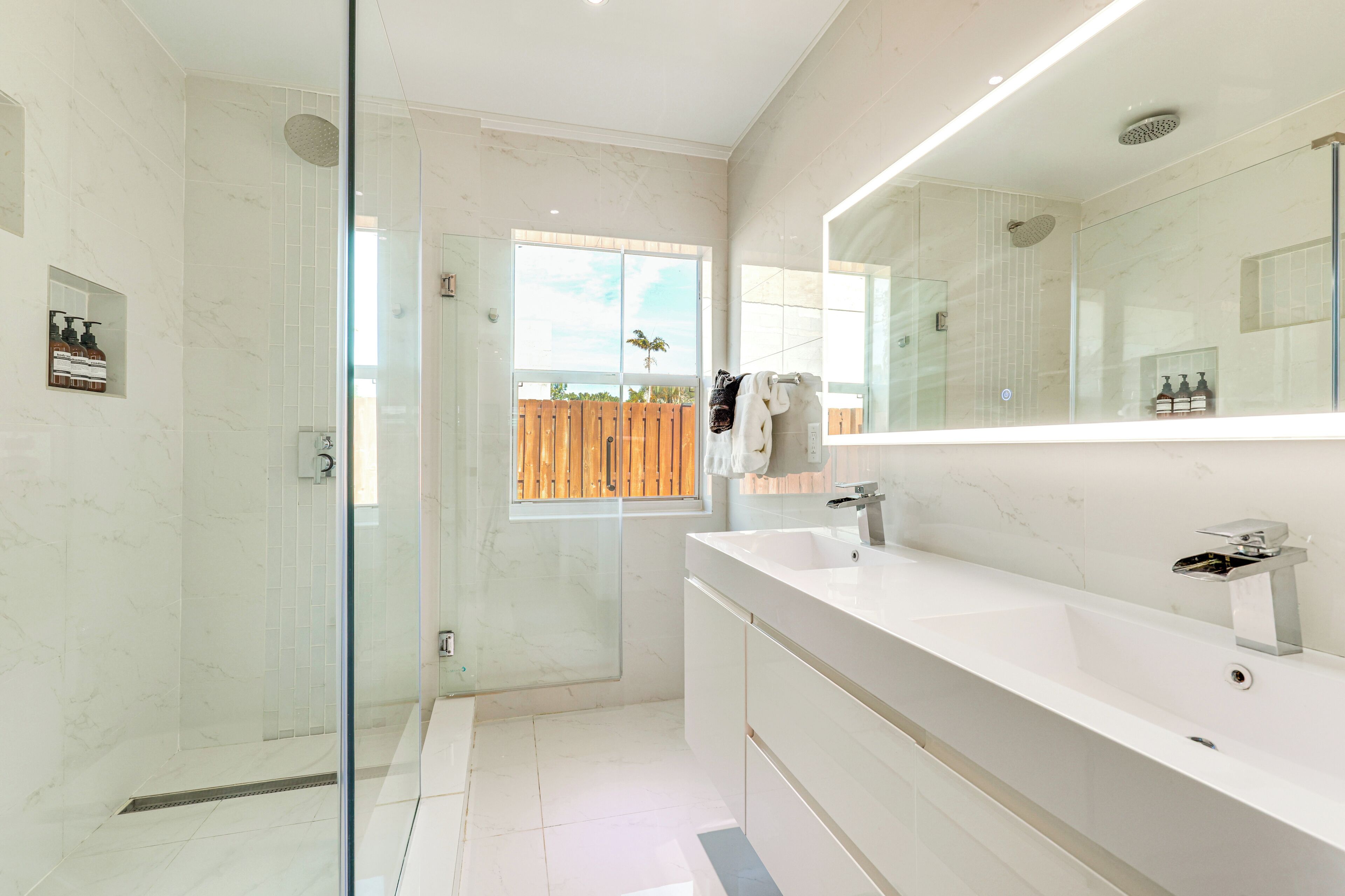 A modern bathroom with a glass-enclosed shower, a large mirror, and a white vanity.