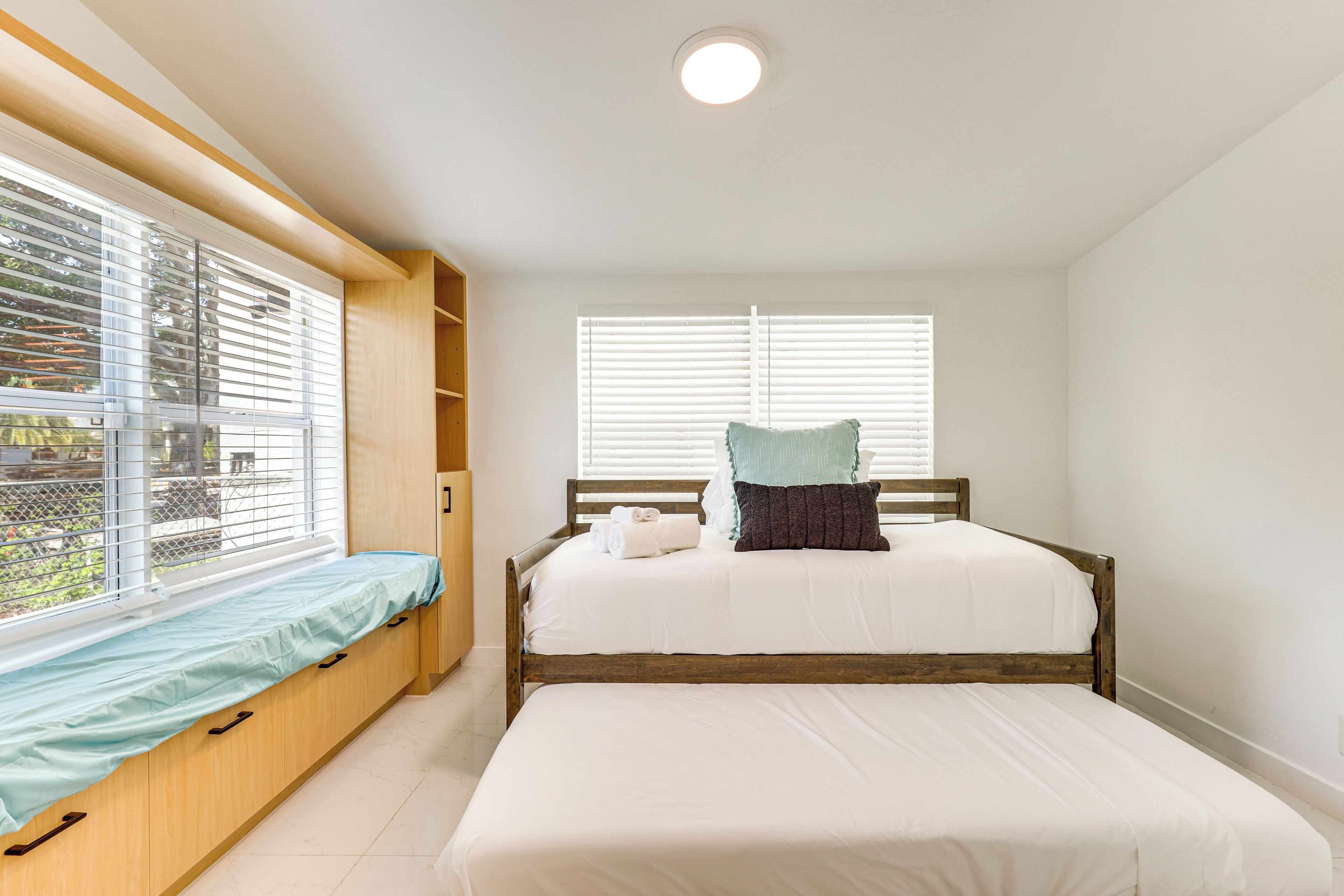 A bedroom with a bed, a bench, and a window with blinds.