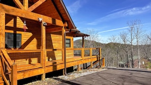 A wooden cabin with a balcony, large windows, and a view of the surrounding forest. - Heavenly View | 4BR • 2 Fireplaces • Brand New in 2026! (Sevierville)