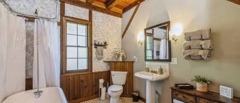 Baño con bañera, inodoro y lavamanos, con vigas de madera y suelo estampado.