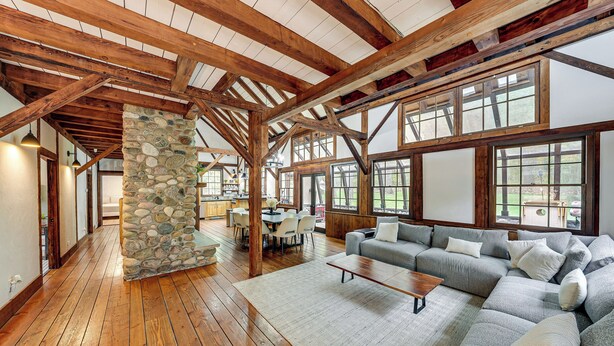 A spacious living area with a stone pillar, wooden beams, a large sectional sofa, and a dining table with chairs. - Tranquil Manor! Lake Geneva English Tudor Estate (Lake Geneva)
