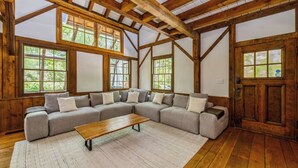 A large L-shaped sectional sofa with a wooden coffee table in a room with exposed wooden beams and large windows. - Tranquil Manor! Lake Geneva English Tudor Estate (Lake Geneva)