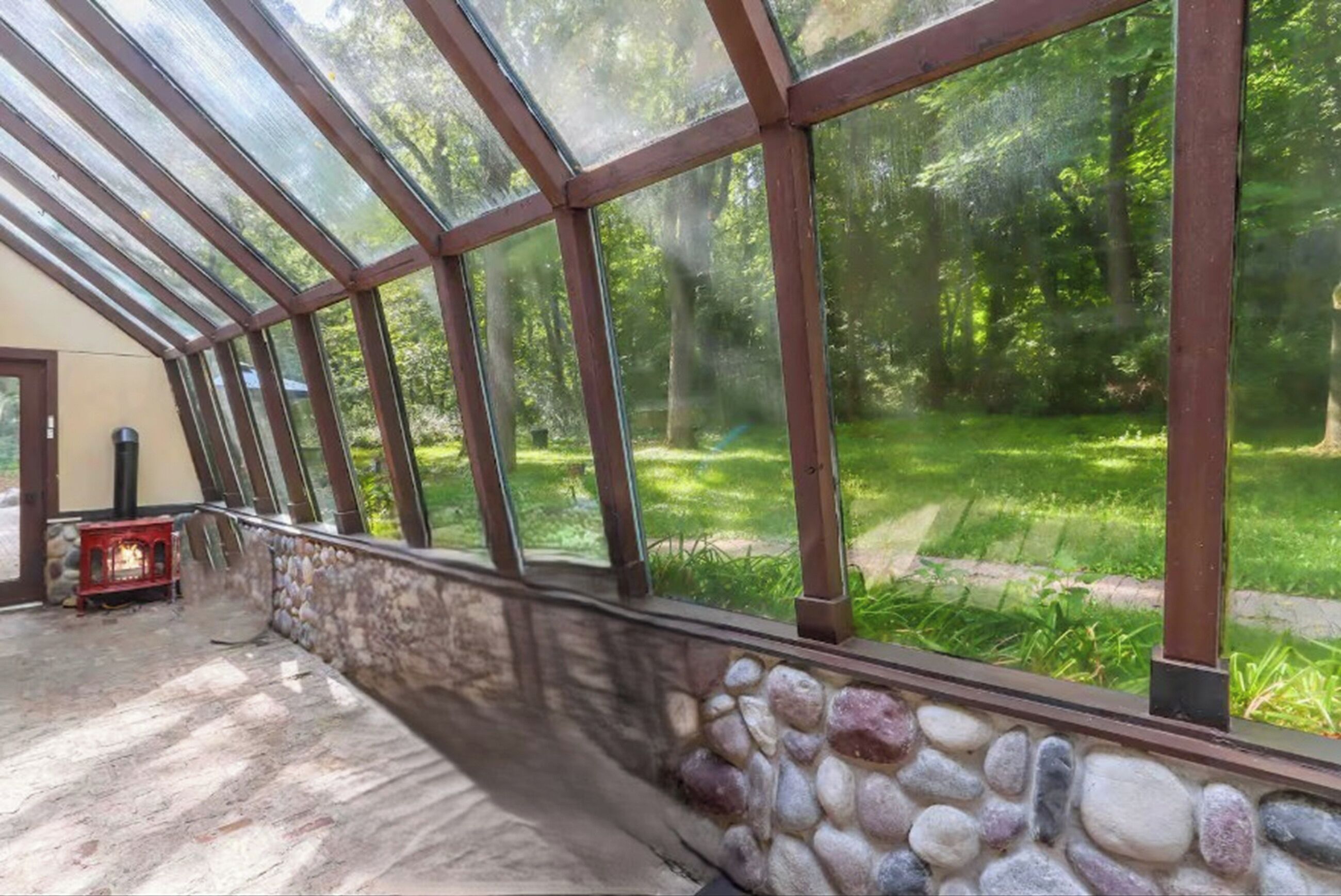 Une véranda dotée d’un mur en pierre et de panneaux de verre, donnant sur un jardin luxuriant.