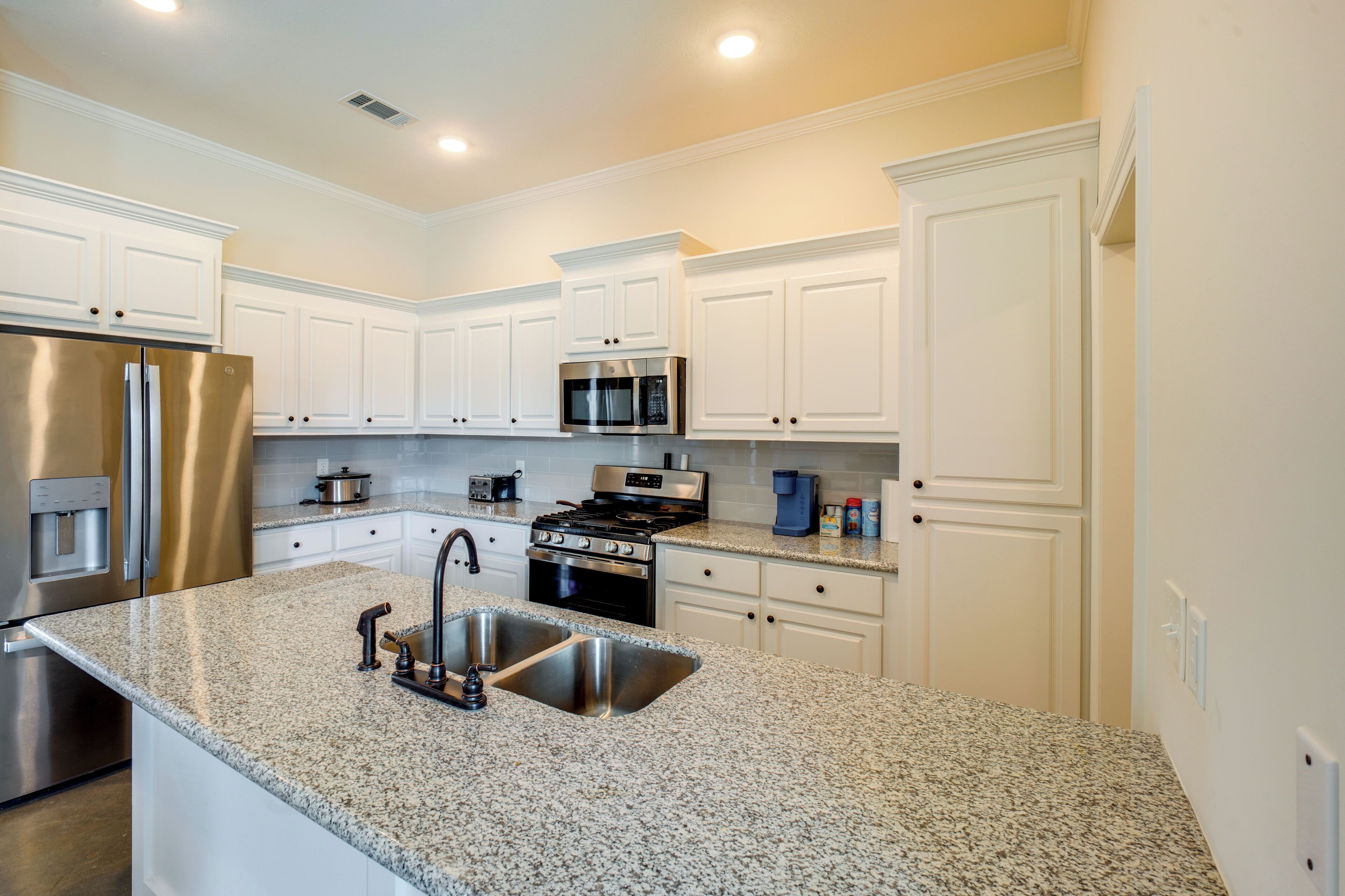 Una cocina moderna con armarios blancos, electrodomésticos de acero inoxidable, encimeras de granito y un lavamanos doble.