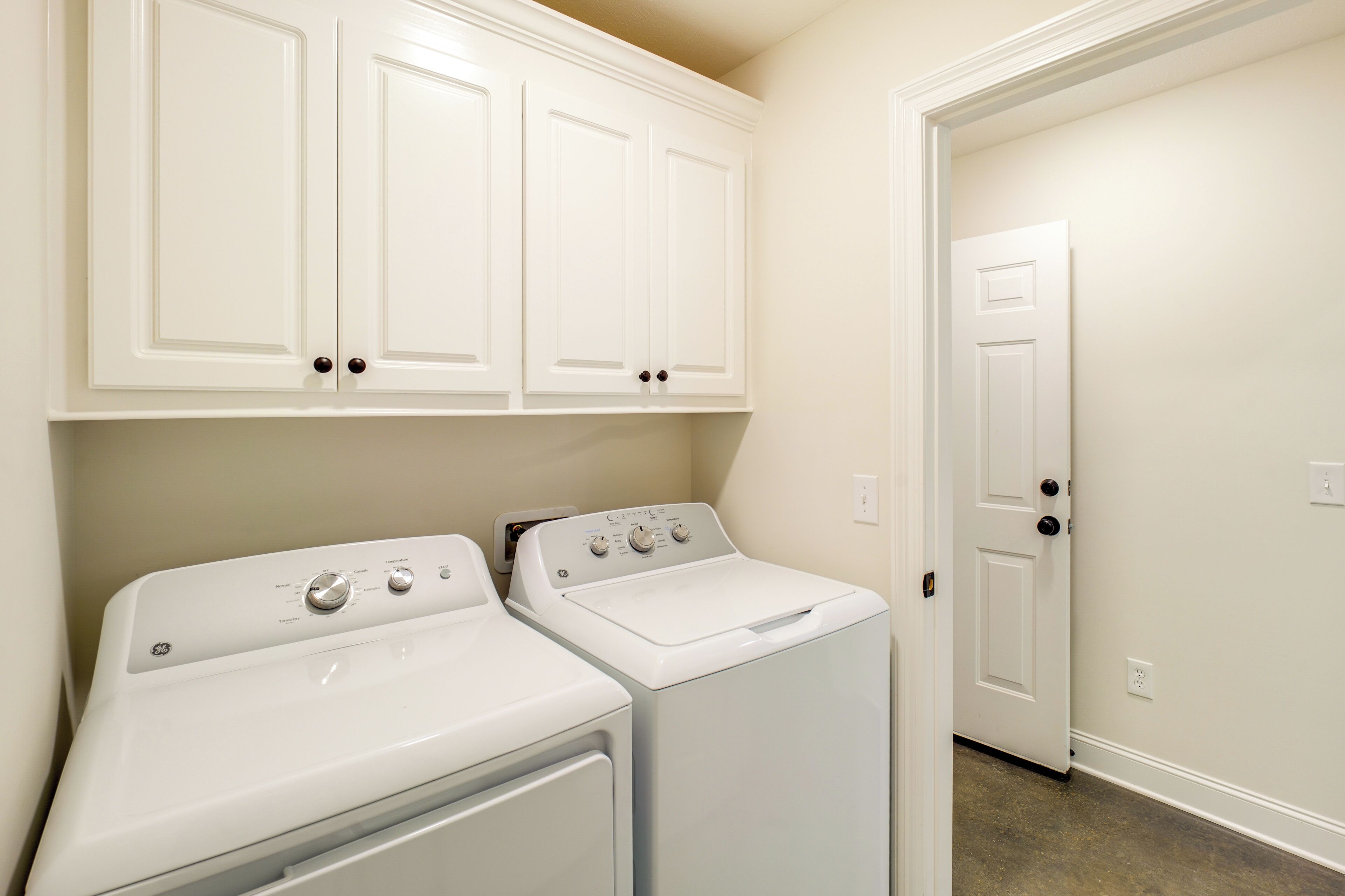 A laundry room with two white washers and dryers, white cabinets above, and a white door in the background.