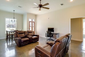 A spacious living room with a brown leather sofa, a dining area with a table and chairs, a ceiling fan, and a television.