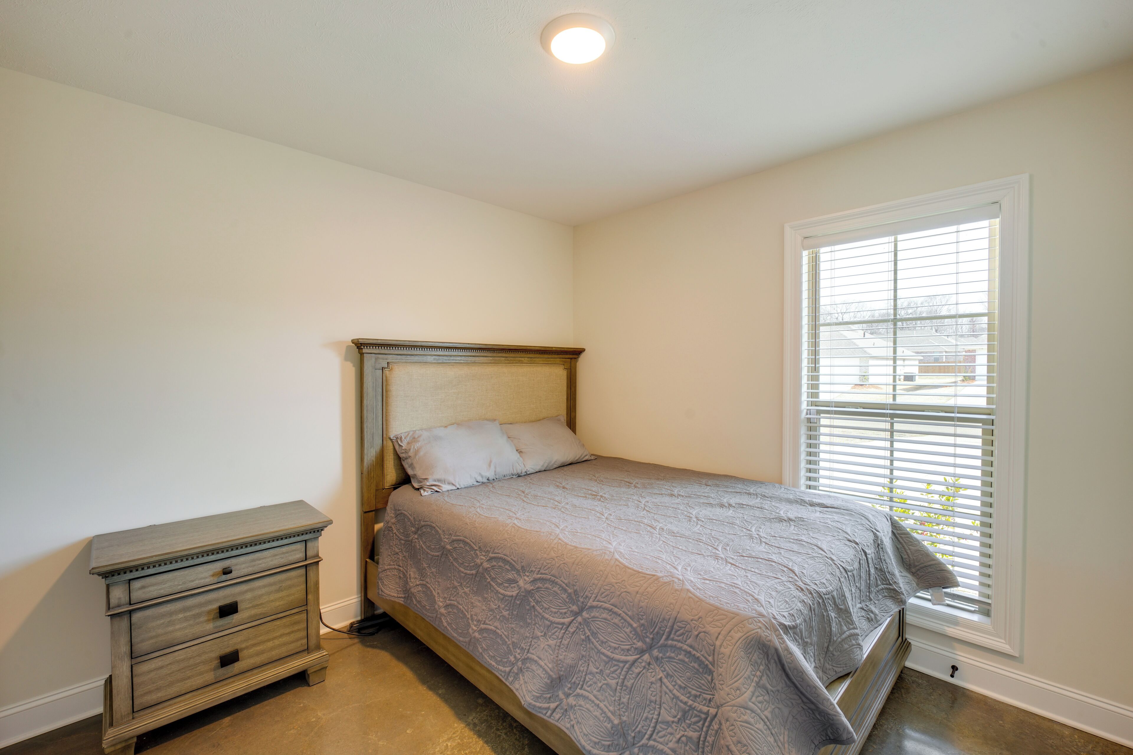A bedroom with a bed, a nightstand, and a window with blinds.