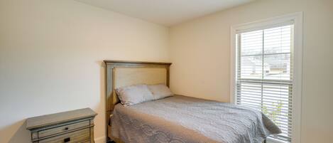 A bedroom with a bed, a nightstand, and a window with blinds.