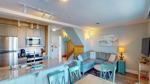 A modern kitchen with granite countertops, stainless steel appliances, and a dining area with a light blue sofa and matching chairs. - Villa 312 3 bedroom, 2 bathroom (Jekyll Island)