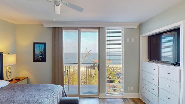 Una camera da letto con un letto, un comodino, una lampada, una TV, una cassettiera e un balcone con vista sull'oceano.