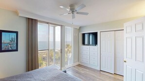 Camera da letto con balcone, ventilatore a soffitto, televisore e armadio.