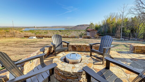 Un foyer en pierre, entouré de fauteuils Adirondack, avec vue sur un lac et des collines lointaines.