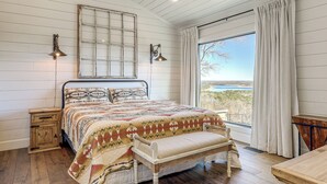 Une chambre à coucher avec un lit en bois, un banc, une table de chevet, une fenêtre avec des rideaux et une vue sur l’extérieur.