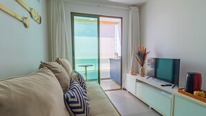 En moderne stue med sofa, et fladskærms-TV og en balkon med et bord.