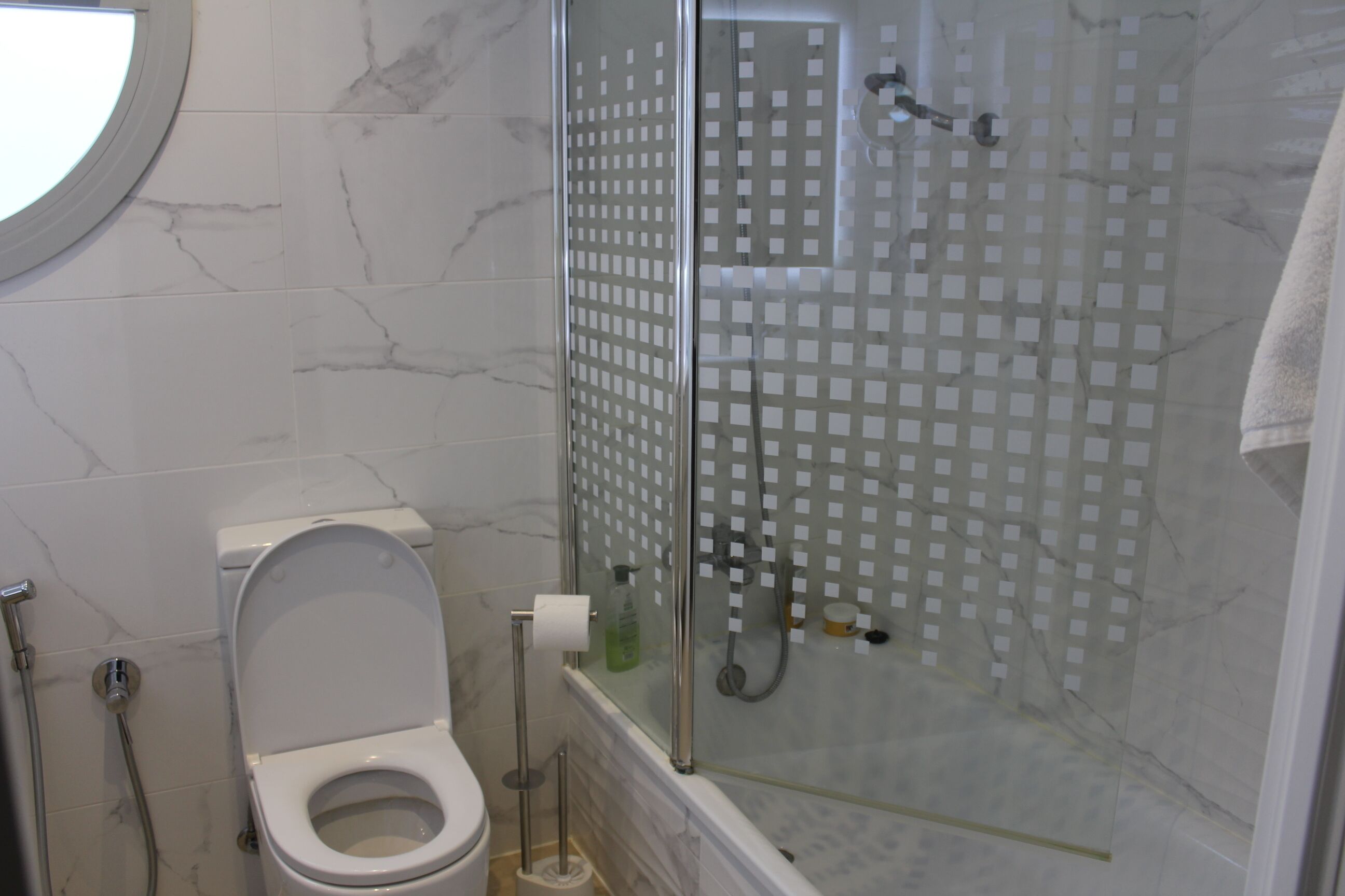 A bathroom with a toilet, a glass shower enclosure, and a marble-tiled wall.