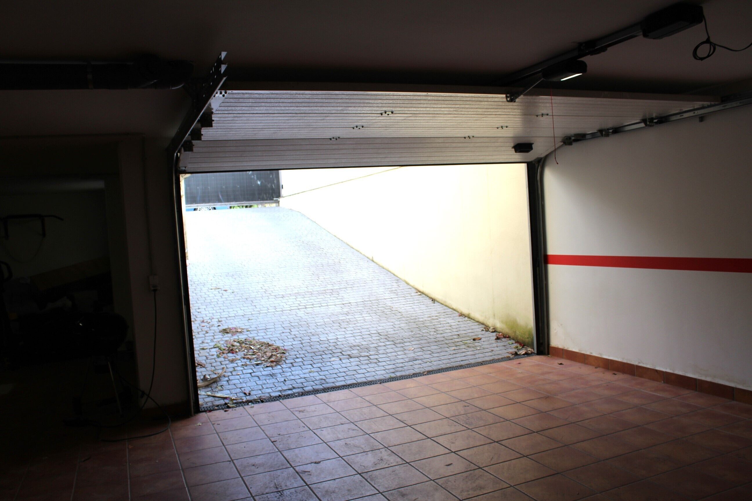An open garage door leading to a paved area with a tiled floor.