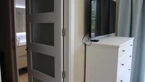 Ein Zimmer mit einem weißen Schrank, einem flachbildfernseher an der Wand und einer Tür zu einem Badezimmer.
