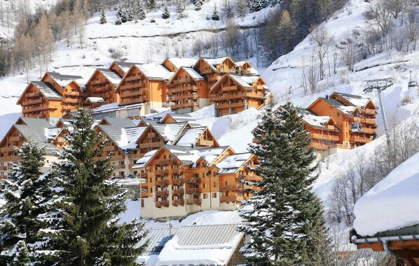 Eine Gruppe Holzhütten mit Balkonen, umgeben von schneebedeckten Bäumen und einer Berglandschaft.