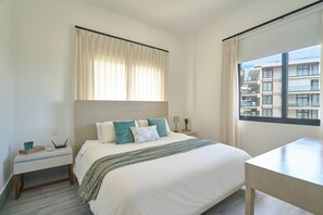 Ein Hotelzimmer mit Bett, Schreibtisch, einem Fenster mit Vorhängen und Blick auf Gebäude.