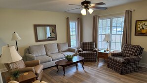 Ein Wohnzimmer mit einer Couch, Sesseln, einem Couchtisch, einem Deckenventilator und großen Fenstern.