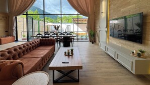 Uma sala de estar moderna com uma janela ampla, um sofá, uma mesa de jantar e uma TV fixada na parede.