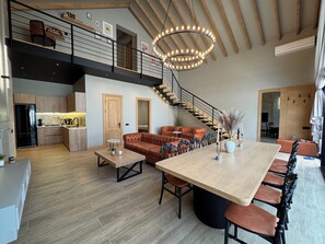 A spacious living area with a large wooden dining table, a leather sofa, and a staircase leading to an upper level. - Luxury Twin Barnhouse Gabala (Gebele)