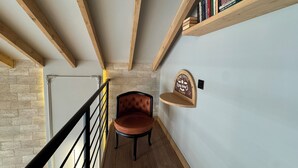 Um corredor estreito com vigas de madeira, uma cadeira, uma estante e uma placa decorativa.