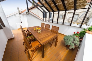 A wooden table with chairs, a tiled floor, and potted plants on a balcony with a view of buildings. - Heritage Home Cvita in Murter (Murter-Kornati)
