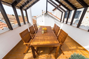 A covered outdoor dining area with a wooden table and chairs, a bowl of fruit, and a view of the surrounding buildings. - Heritage Home Cvita in Murter (Murter-Kornati)
