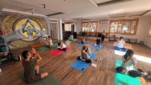 Un cours de yoga dans une salle dotée de planchers en bois, de grandes fenêtres et d’une tapisserie.