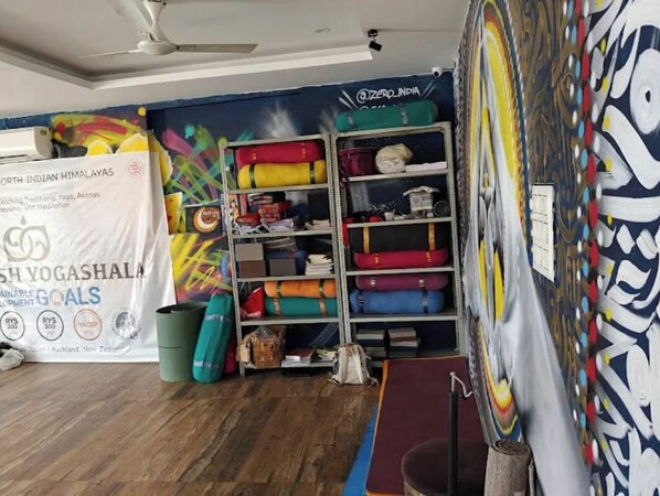 A yoga studio with a mural, a shelf with yoga mats, and a banner advertising yoga and meditation. - Yog Namah Hotel & Cafe (Rishikesh)