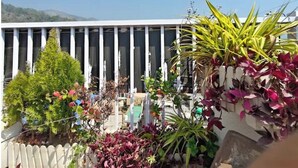 Un balcon doté d’une balustrade blanche, de différents pots de plantes et offrant une vue sur un bâtiment orné de colonnes verticales.