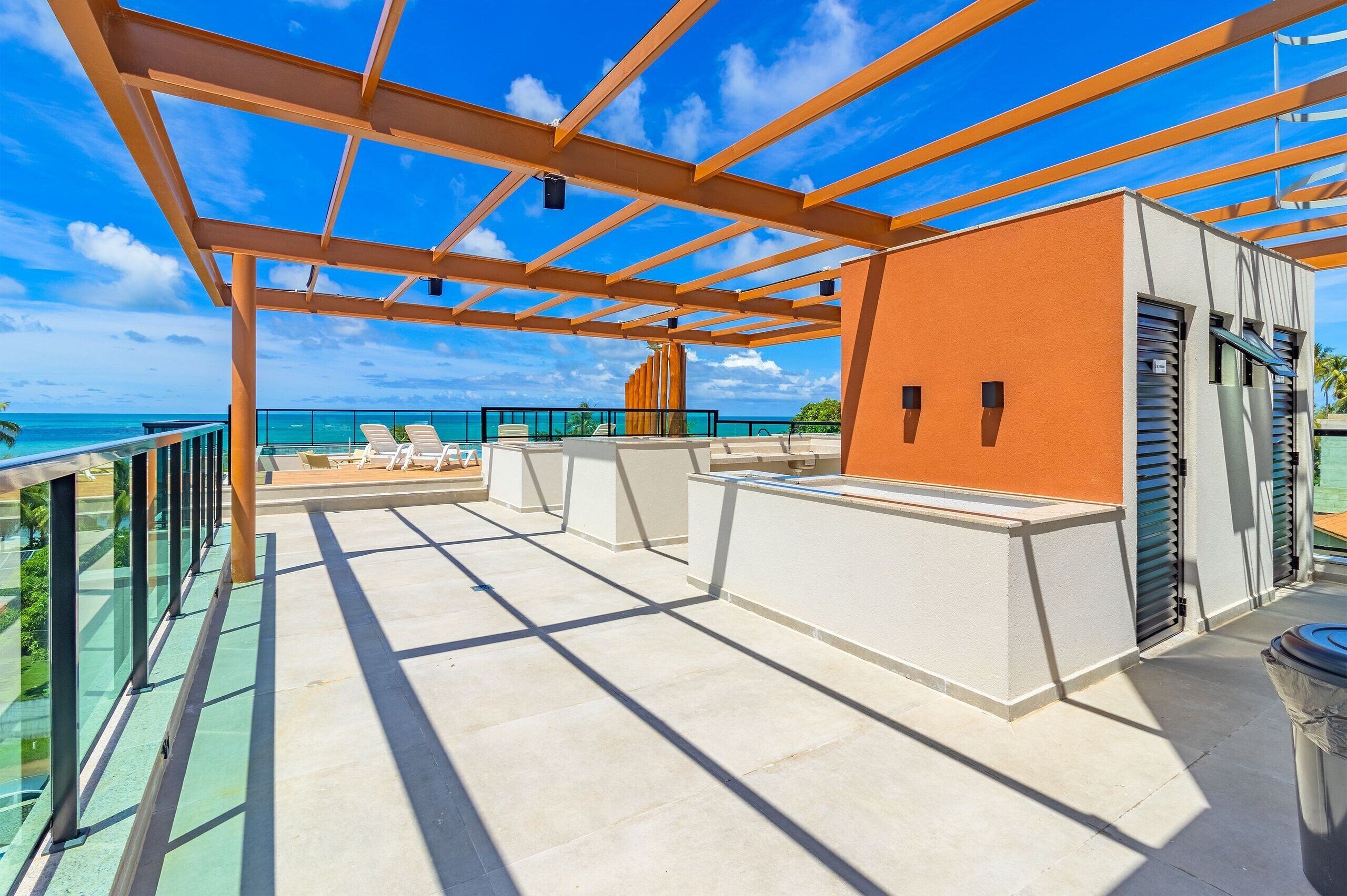 Terraço no telhado com vista desobstruída para o oceano, estrutura de pérgola e área de estar com cadeiras brancas.
