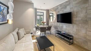 A modern living room with a sofa, coffee table, TV, and dining area with chairs and a table. - Spacious XXL Deluxe suite with private balcony and village views. (Bad Gastein)