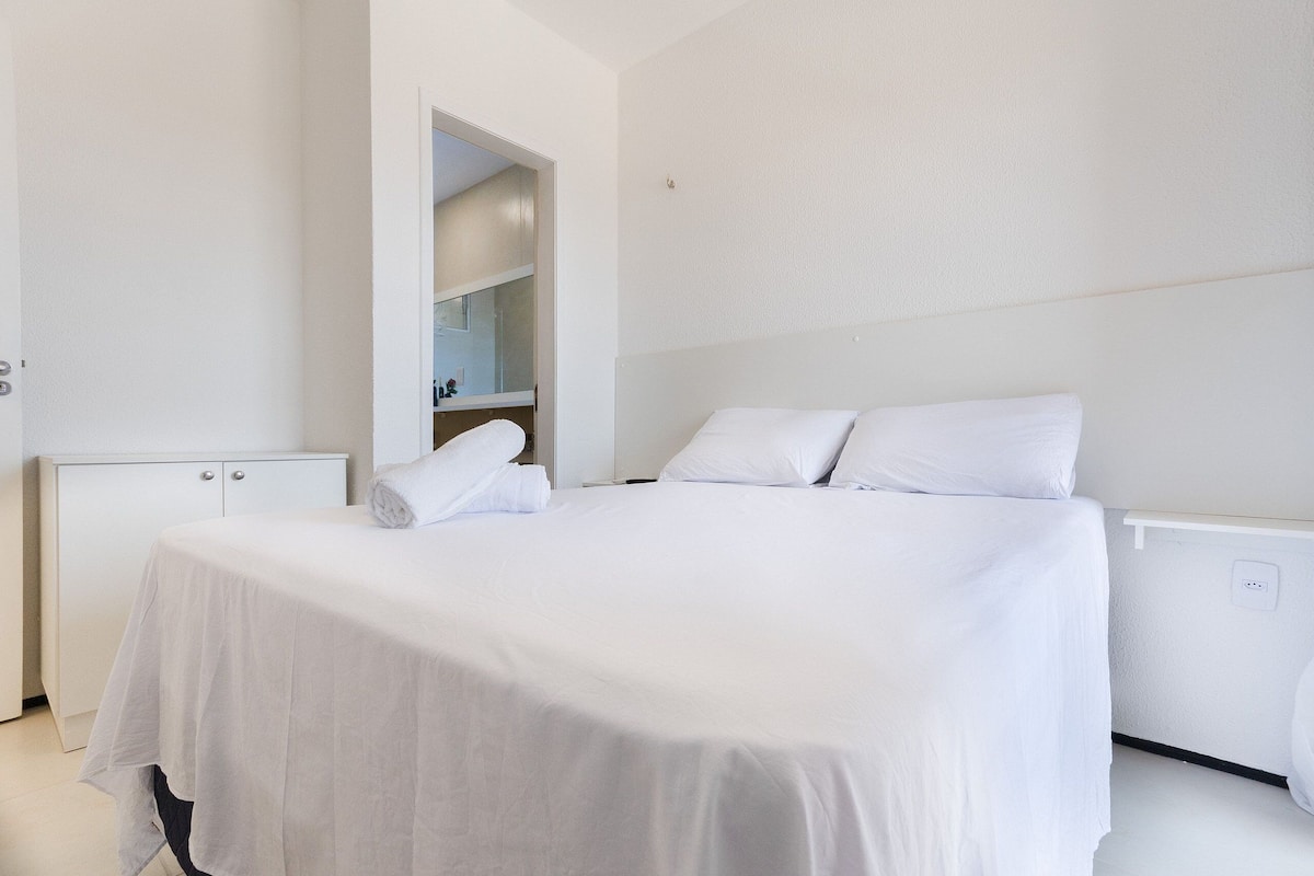 Ein sauberes, weißes Hotelzimmer mit einem Bett, einem kleinen Schrank und einer eingebauten Ablagefläche.