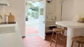 Una cocina con encimera blanca, lámpara colgante y puerta que da al exterior.