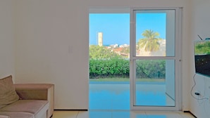 A room with a sliding glass door leading to a balcony with a view of palm trees and buildings. - Beach Townhouses - Porto das Dunas By Carpediem (Aquiraz)