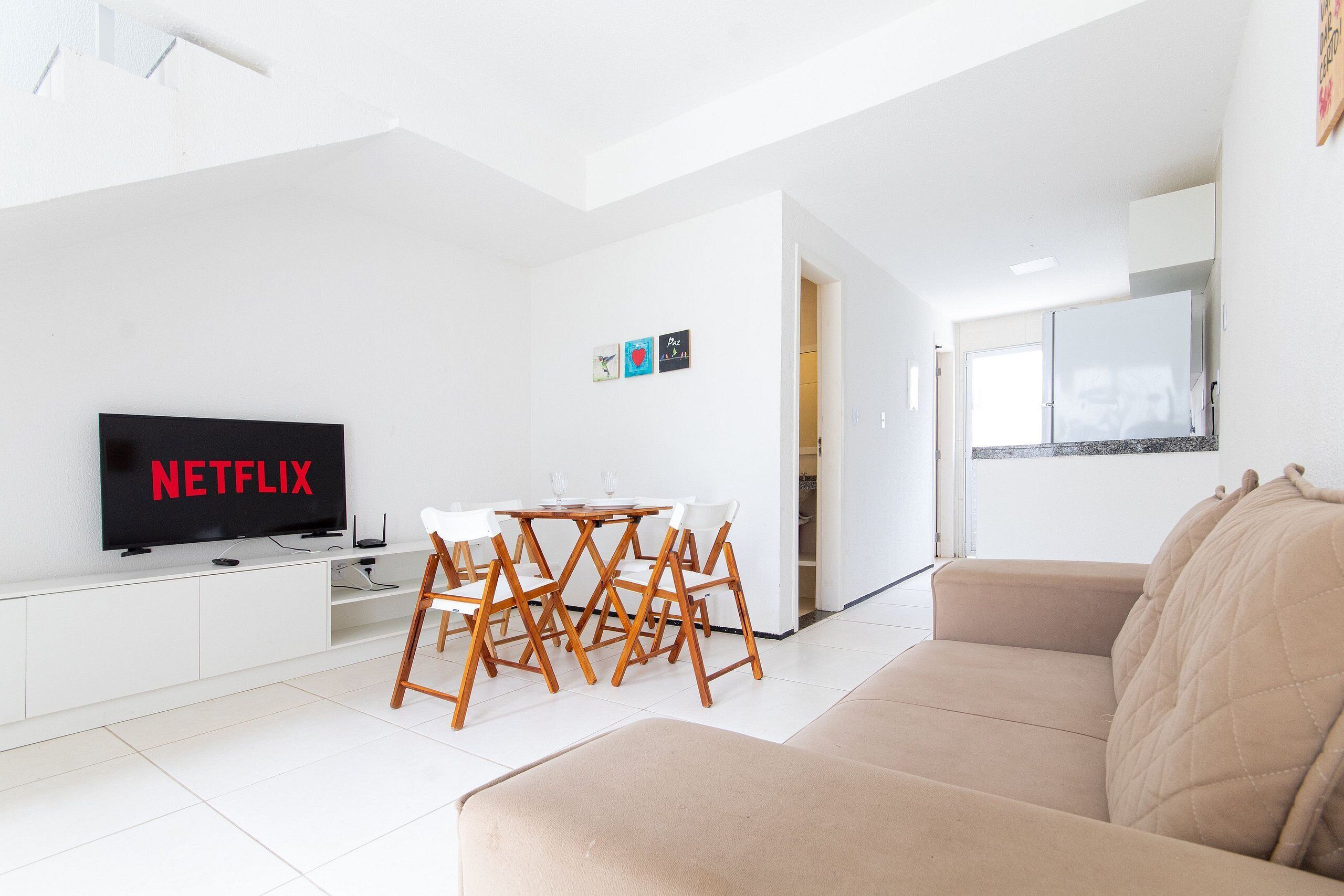 A modern living room with a flat-screen TV, a dining table, and a beige sofa.