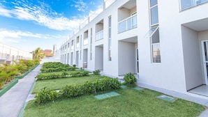 A modern building with multiple balconies, a well-maintained lawn, and a clear sky. - Beach Townhouses - Porto das Dunas By Carpediem (Aquiraz)