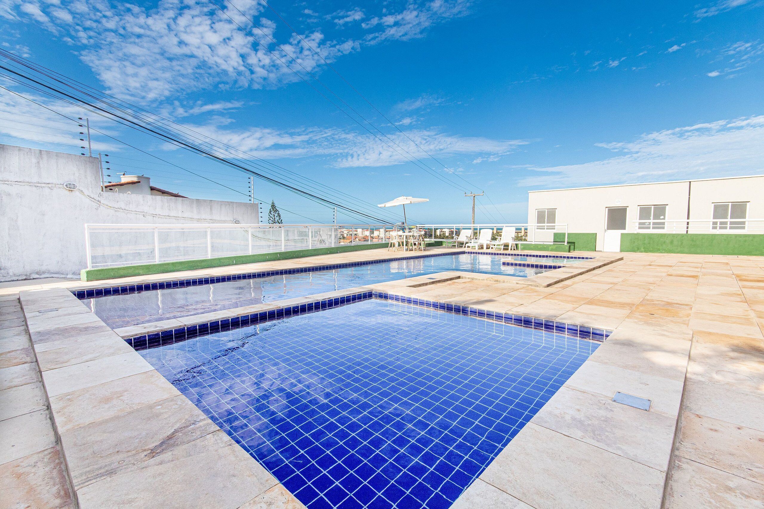 A swimming pool with blue tiles, surrounded by a tiled deck, and a building with large windows in the background.
