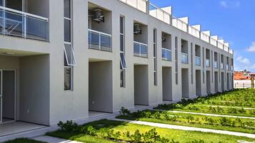 A modern building with a linear facade, multiple balconies, and a well-maintained garden area.